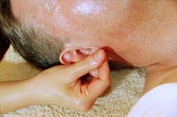 Wellnessmassage: Indische Marma Massage. Eine Frauenhand massiert das Ohrläppchen